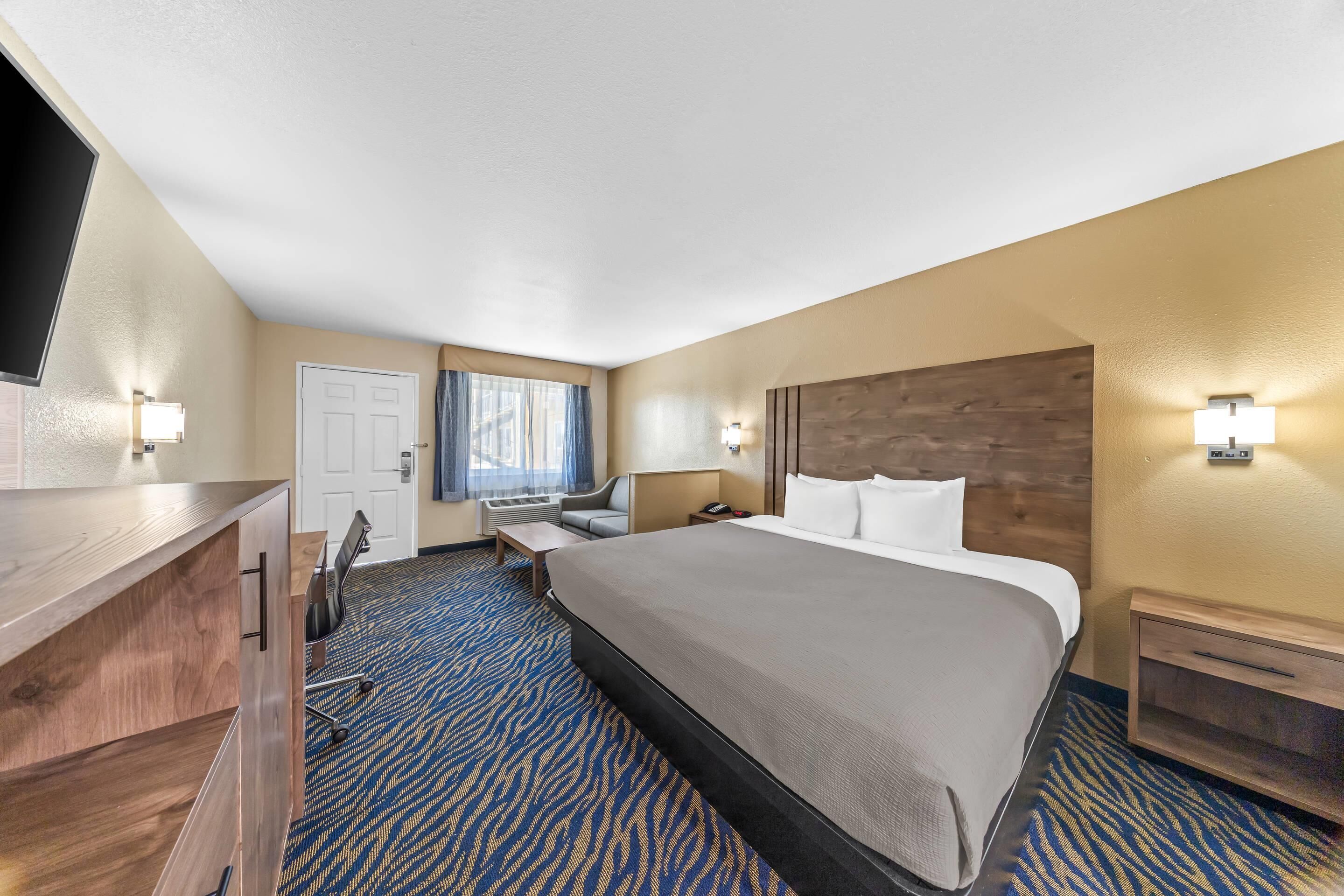 A hotel room with a large bed, a desk, a chair, a TV, and a window with curtains.