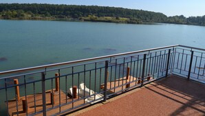 Une terrasse au bord du lac, dotée d’une rambarde en métal, de sièges et offrant une vue sur le lac et la zone boisée.