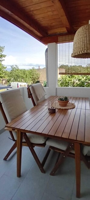 A wooden table with chairs, a potted plant, and a hanging light fixture in a covered outdoor area.