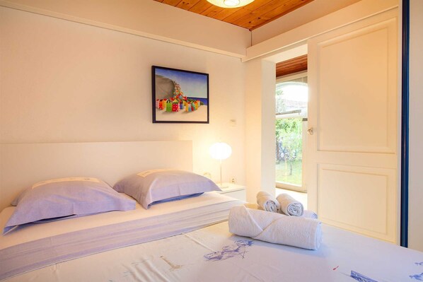 A bedroom with a bed, pillows, a bedside lamp, a window, and a painting on the wall.