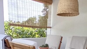 Et træbord med stole, en hængende vævet lampe, og udsigt til grøn bevoksning udenfor.