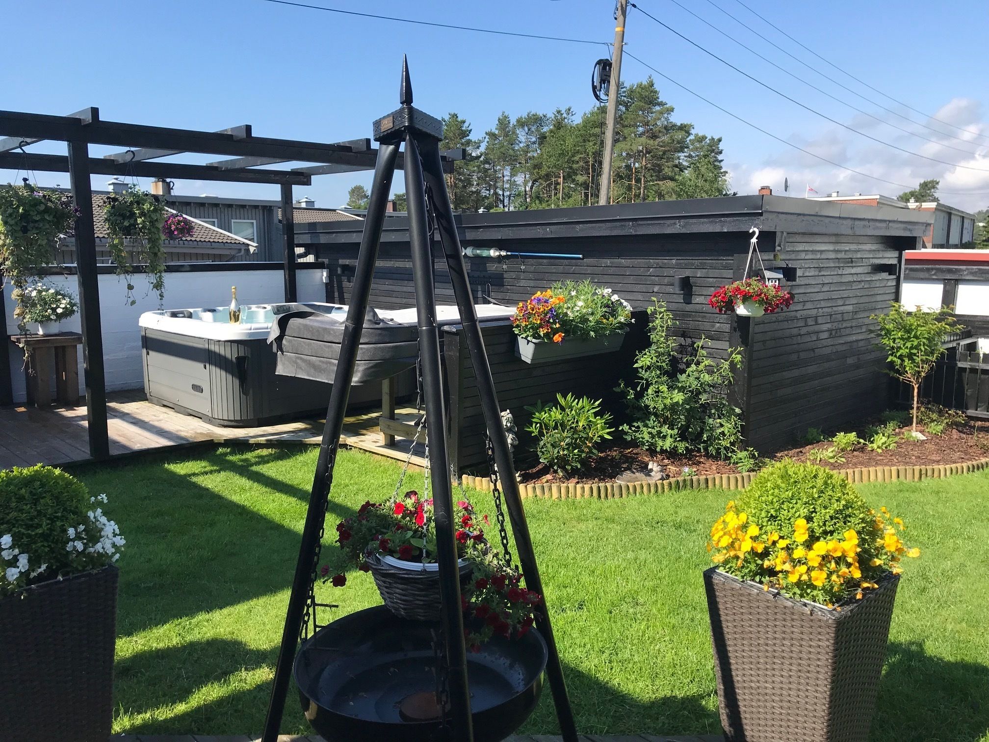 Un patio trasero con un jacuzzi, una pérgola y diversas plantas en macetas.