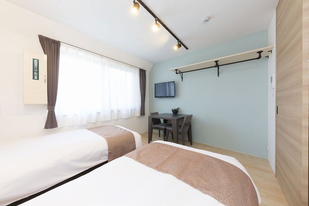 A hotel room with two beds, a desk, a chair, a TV, and a window with curtains.