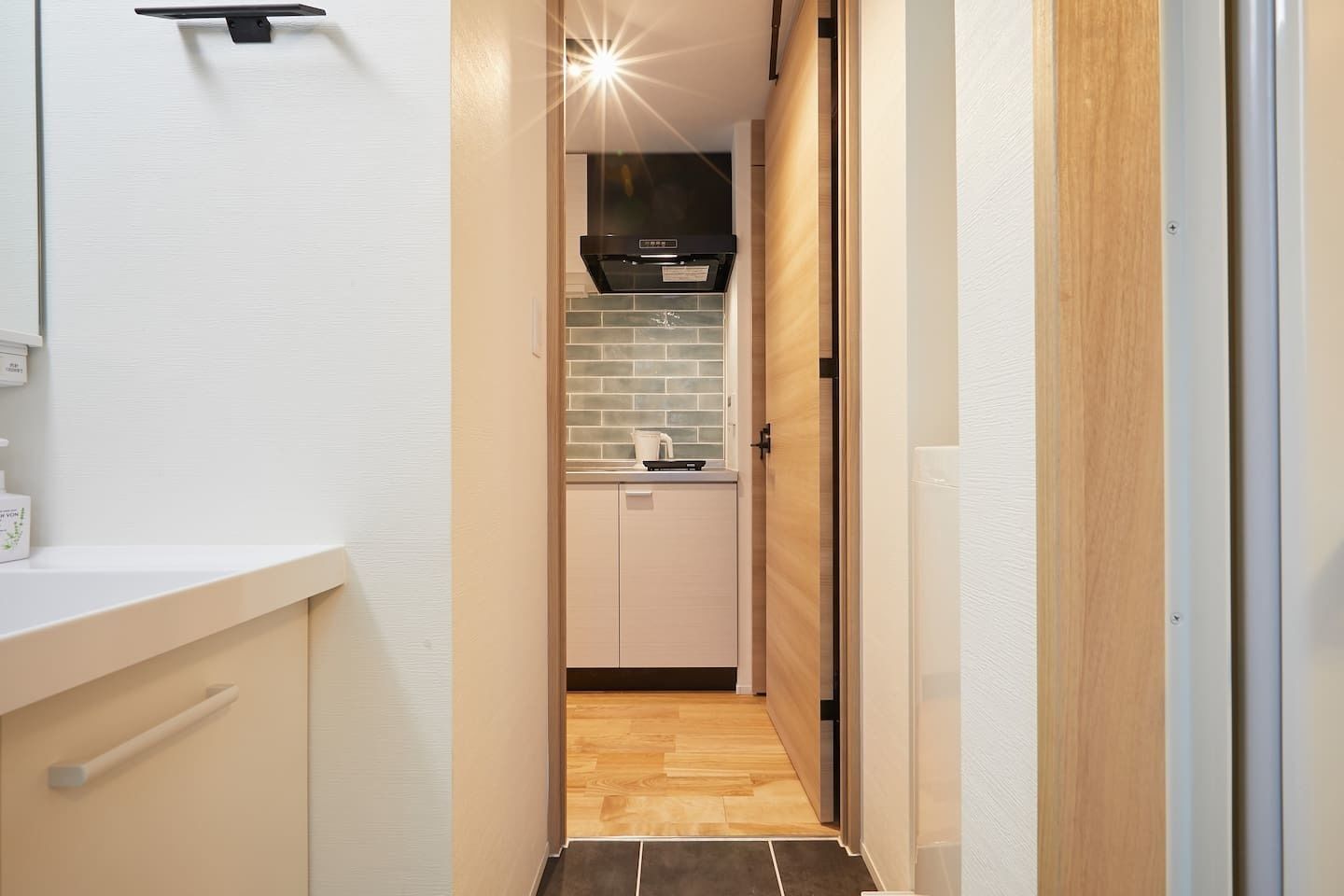 A narrow hallway leading to a kitchen with a tiled backsplash and wooden cabinets.