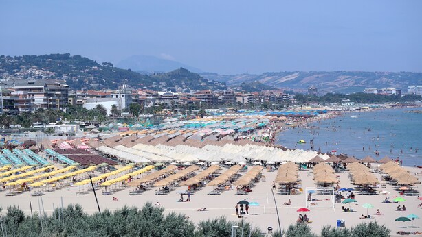 A beach with rows of umbrellas and sun loungers, a clear sky, and buildings in the background. - Nice Property throughout August (Pescara)