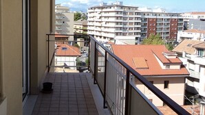A balcony with tiled flooring and a metal railing, overlooking a residential area with multi-story buildings and a clear sky. - Nice Property throughout August (Pescara)