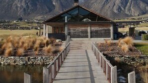 Un ponte di legno conduce a un edificio con tetto in vetro, immerso tra montagne e un lago.