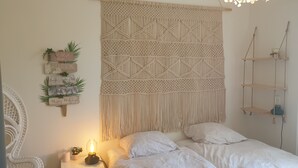 A bedroom with a macrame wall hanging, a bed with white bedding, a bedside table with a lamp, and a shelf with decorative items. - Large country house with swimming pool, SPA, terrace, garden, WIFI access 5 min from Sanary  (Ollioules)