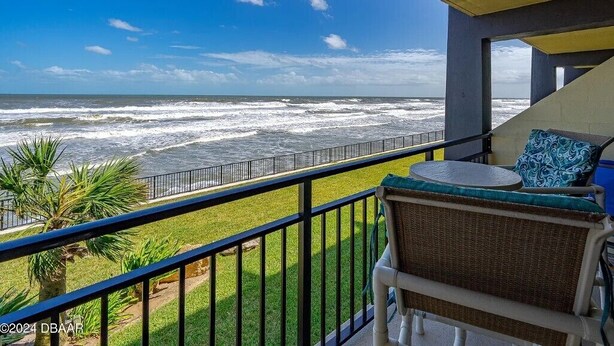 A balcony with a view of the ocean, a chair with a cushion, and a railing.