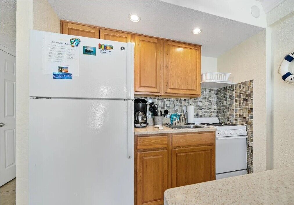 Una cocina compacta con armarios de madera, un refrigerador blanco, una estufa y un salpicadero de azulejos.