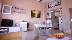 A living room with a TV, dining table, chairs, and a fruit bowl.