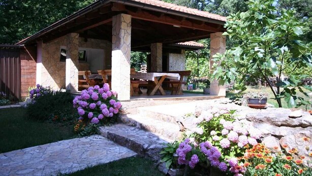 A stone building with a covered patio, outdoor seating, and a garden with flowers.