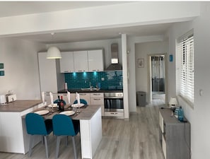 A modern kitchen with a central island, a dining area with blue chairs, and a shower area. - Stunning, fully refurbished apartment in small, exclusive complex with pool (Kotor)