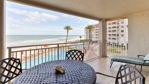 Een balkon met uitzicht op het strand en de zee, een zwembad en tuinmeubilair.