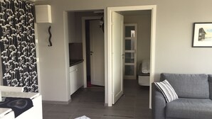 A modern living room with a grey sofa, a kitchen area with white cabinets, and a dining area with a table and chairs. - Functional apartment with sea view (Tanum)