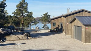 A building with a gravel driveway, wooden exterior, and a view of a lake. - Functional apartment with sea view (Tanum)