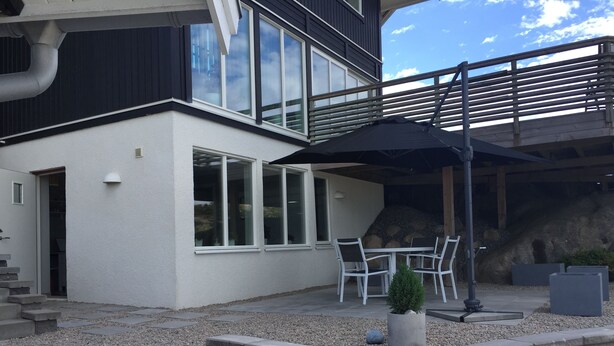 A modern house with a patio area featuring a table and chairs, a small potted plant, and a stone wall. - Functional apartment with sea view (Tanum)
