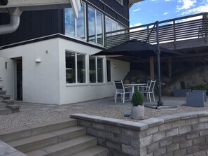 A modern house with a patio area featuring a table and chairs, a small potted plant, and a stone wall. - Functional apartment with sea view (Tanum)