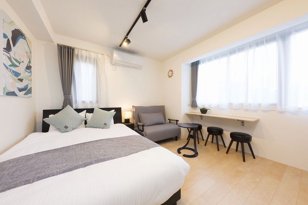 A bedroom with a bed, a chair, a desk, and two stools.