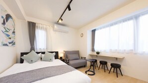 A bedroom with a bed, a chair, a desk, and two stools. - B1  Maison Philippe Shitaya 201 (Tokyo)