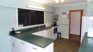 Une cuisine de taille réduite, dotée d’un plan de travail vert, de meubles blancs, d’une cuisinière et d’un évier.