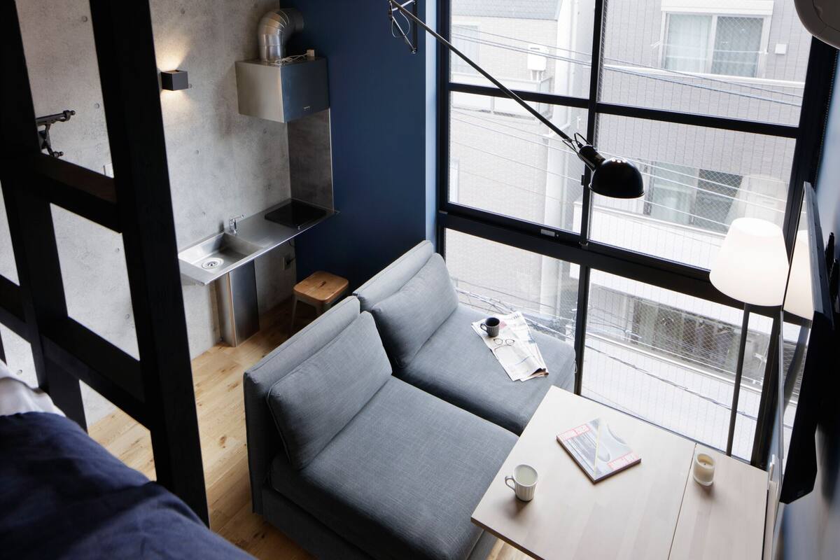 A compact living space with a grey sofa, a small wooden table, and a window with a view of buildings.