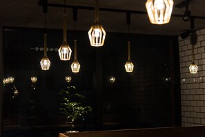 A dark interior with multiple hanging pendant lights and a potted plant. - Hotel Arcsens (Tokyo)