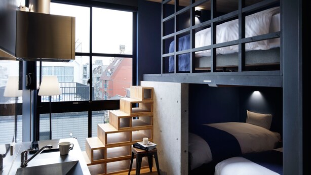 A compact room with a bunk bed, a desk with a sink, and a window with a view of buildings. - Hotel Arcsens (Tokyo)