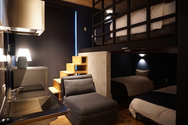 A compact hotel room with a bunk bed, a small kitchenette, a sofa, and a desk.