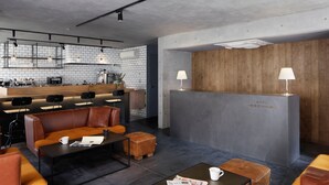 A modern hotel lobby with leather seating, a reception desk, and a kitchen area in the background. - Hotel Arcsens (Tokyo)