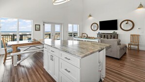 Amplia sala de estar con una isla grande, muebles blancos y un televisor de pantalla plana montado en la pared.