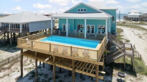 Una casa frente a la playa con piscina, terraza de madera y varios niveles.