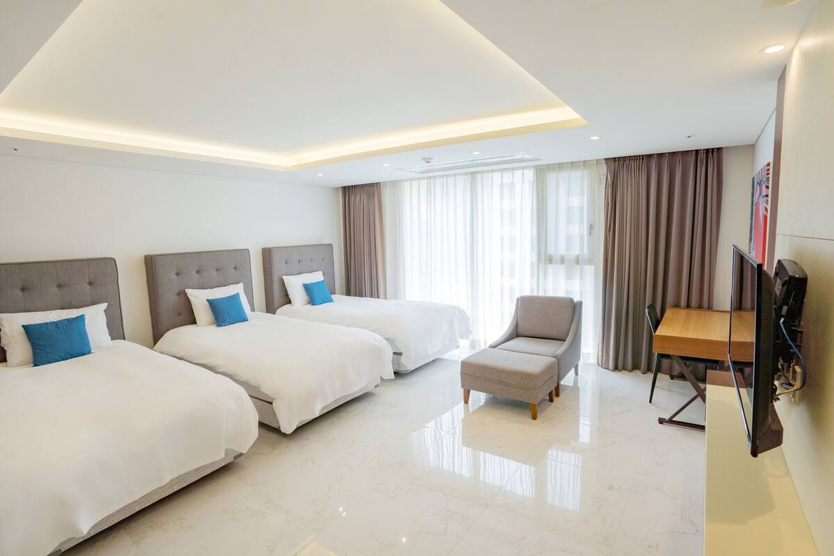 Habitación de hotel con tres camas, televisión, escritorio y una silla.