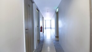 Ein langer, schmaler Flur mit Türen an beiden Seiten, einem an der Wand befestigten Feuerlöscher und einer Deckenleuchte.