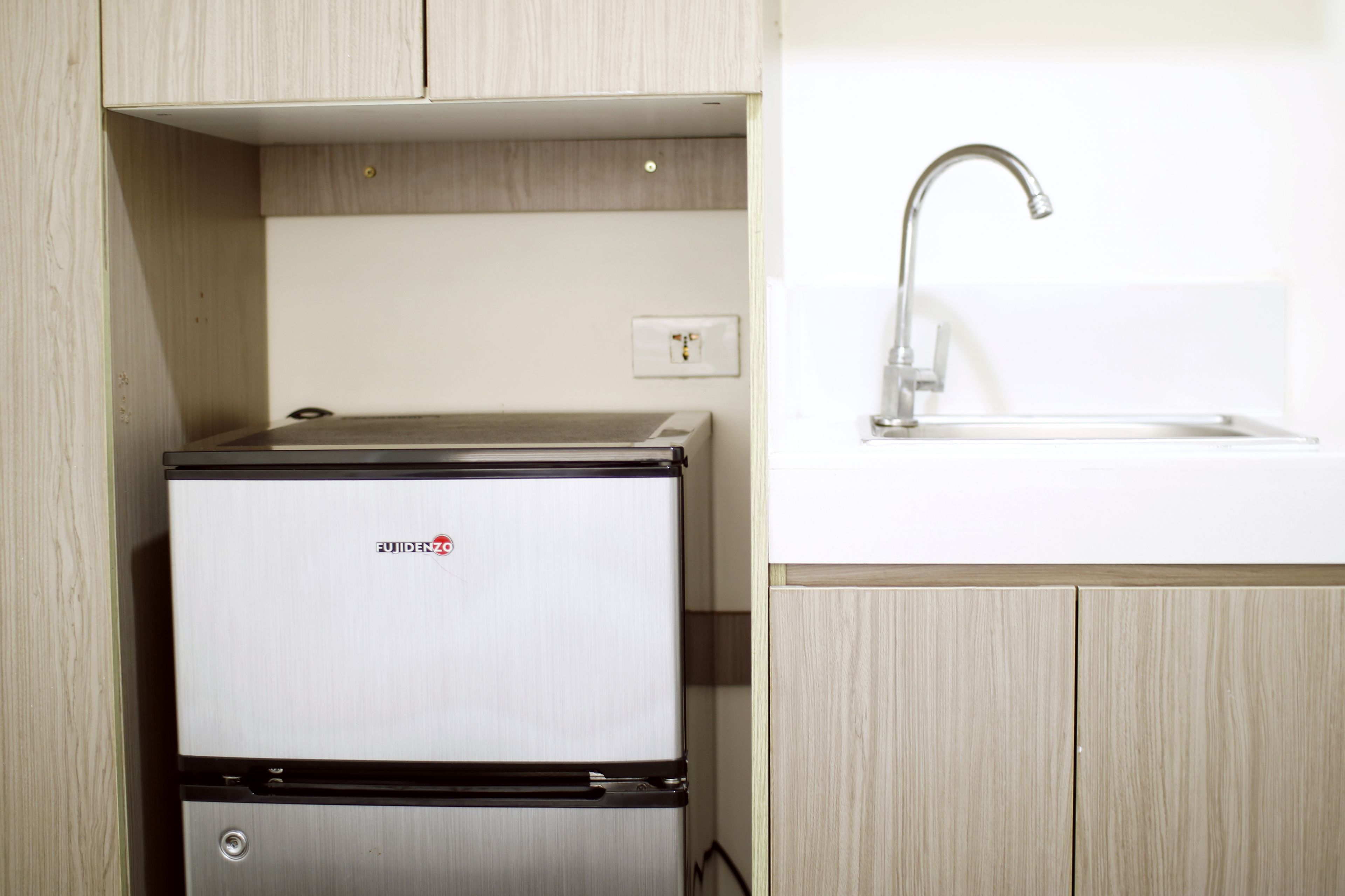 A compact kitchen with a built-in refrigerator, a sink, and wooden cabinetry.