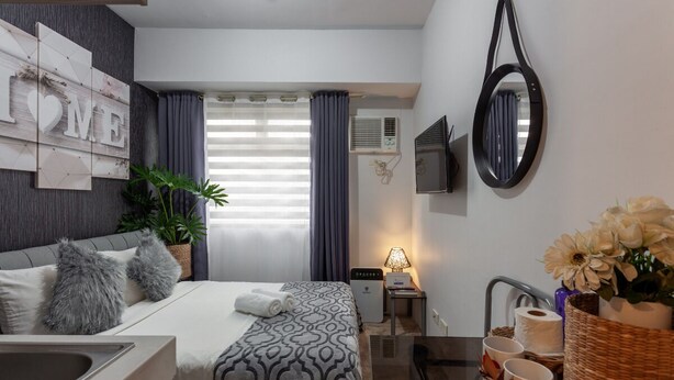 Ein modernes Hotelzimmer mit Bett, Schreibtisch, Spiegel, Pflanze und einem am Wand montierten Fernseher.