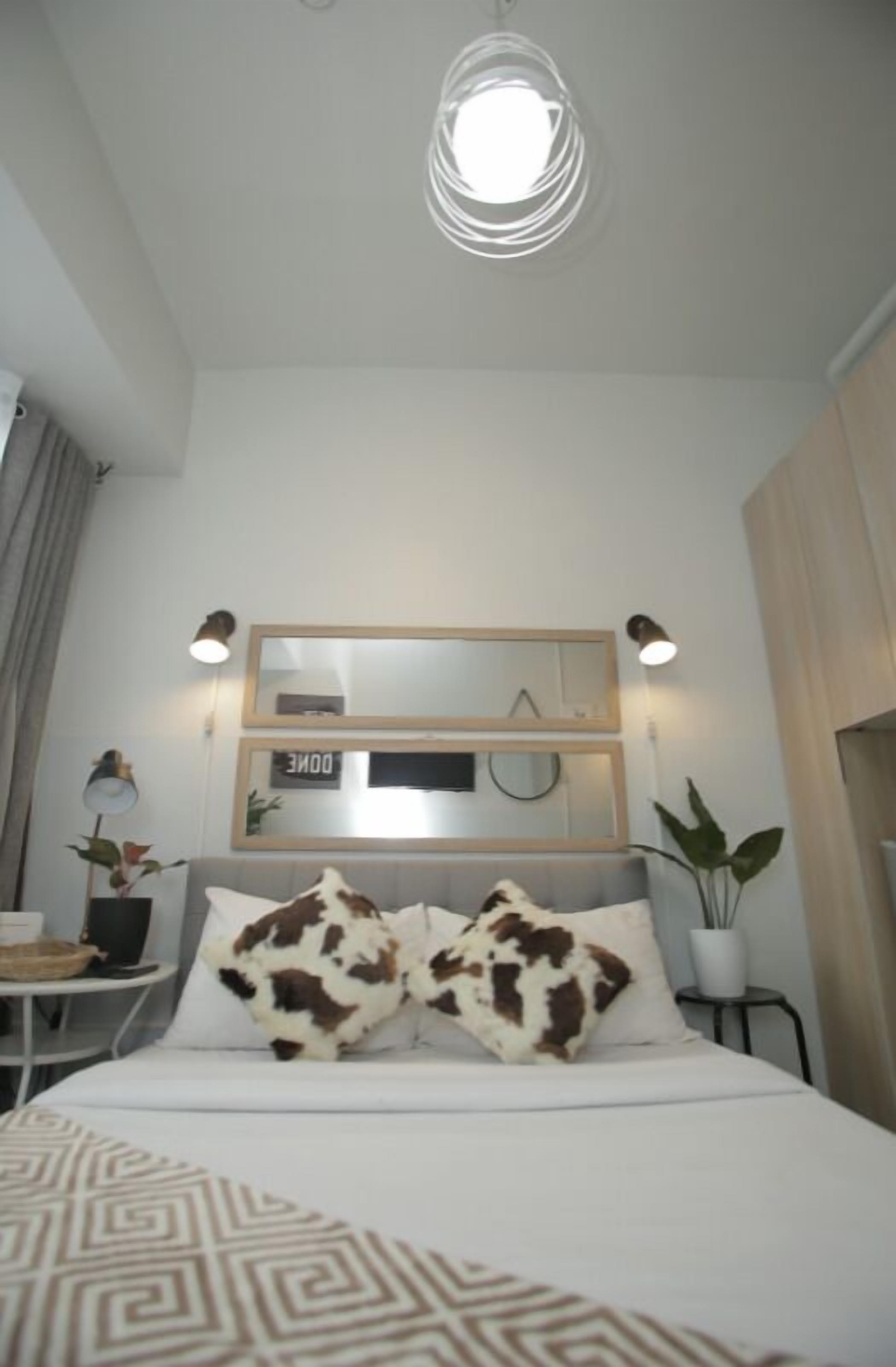 Et pænt indrettet hotelværelse med en seng, et natbord med lampe, et spejl og et vægur.