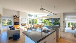 Una cuina moderna amb una illa gran, electrodomèstics integrats i una zona de dinar amb vista a l'exterior.