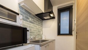 A compact kitchen with white cabinets, a microwave, a stove, and a window. - B3  Maison Philippe Shitaya 302 (Tokyo)
