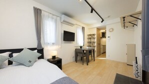 A hotel room with a bed, bedside table, lamp, and a view of the kitchen and dining area. - B3  Maison Philippe Shitaya 302 (Tokyo)