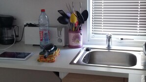 Een keuken met een magnetron, gootsteen en raam met jaloezieën.