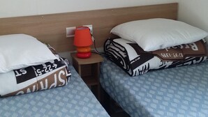 Een hotelkamer met twee bedden, elk voorzien van beddengoed met een patroon, een nachtkastje met een lamp en een plank boven de bedden.