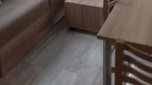 Een ruimtelijk ingerichte leefruimte met een bank, een klein houten tafeltje en een raam met gordijnen.