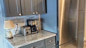 A kitchen with grey cabinets, a stainless steel refrigerator, a toaster, and a coffee maker on the countertop.