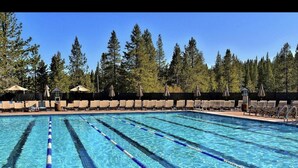 A swimming pool with clear blue water, surrounded by lounge chairs and umbrellas, with trees in the background.