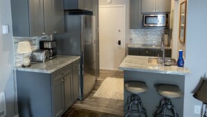 A modern kitchen with grey cabinets, stainless steel appliances, a microwave, and a bar area with stools.