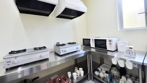 A modern kitchen with stainless steel appliances, including a gas stove, microwave, and a built-in oven. There are hanging utensils and a scale on the counter. - Chura Cabin Kokusai-Dori (Naha)