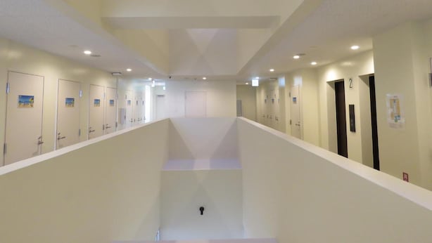 A hotel corridor with multiple doors, a central staircase, and a ceiling with recessed lighting. - Chura Cabin Kokusai-Dori (Naha)