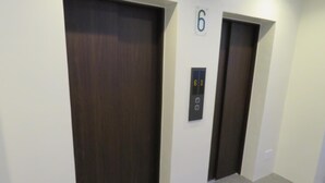 A hallway with two wooden doors and an elevator with a control panel. - Chura Cabin Kokusai-Dori (Naha)