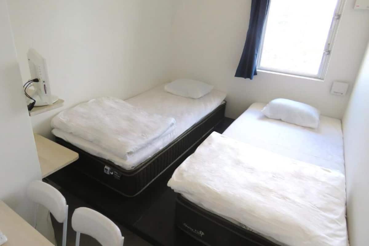 A small, clean room with two single beds, a desk, and a chair.